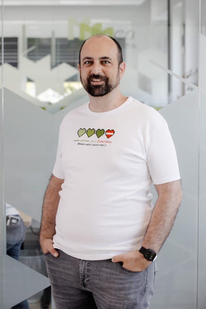 Michael Ulm steht vor einer Glaswand und trägt ein weißes Shirt mit drei grünen Pixelherzen und einem roten Pixelherz.