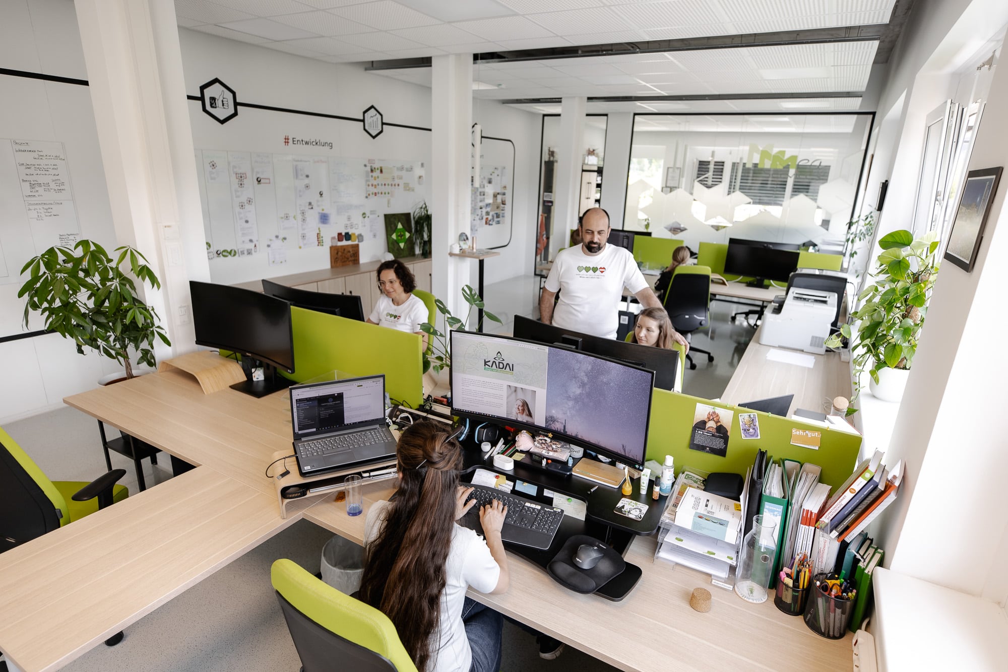 Büroansicht von mea IT Services: weiße Wände, Holztische und grüne Schreibtischstühle